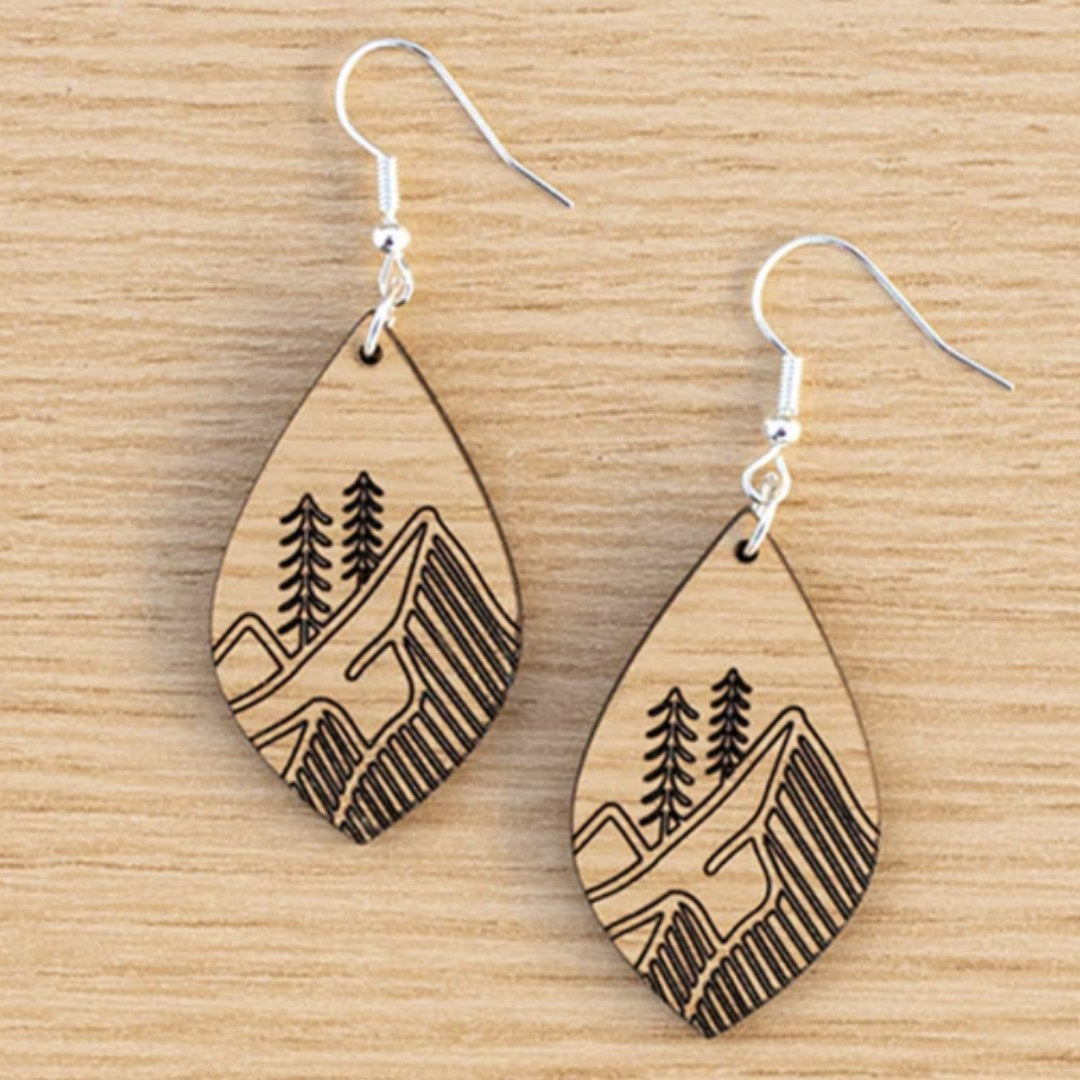 Laser engraved earrings shaped like a leaf with engraved images of mountains and trees. Made with Oak Truflat wood sold by Thunder Laser Canada. Canada Laser Supply
