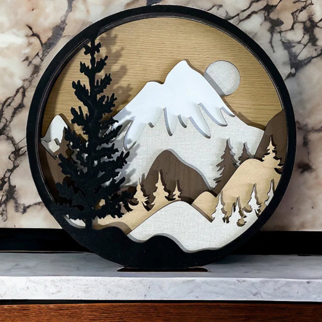A mountain scene with trees on a circular signs many out of different colors of Truflat engineered wood. Sold by Thunder Laser Canada. Laser Supply Canada